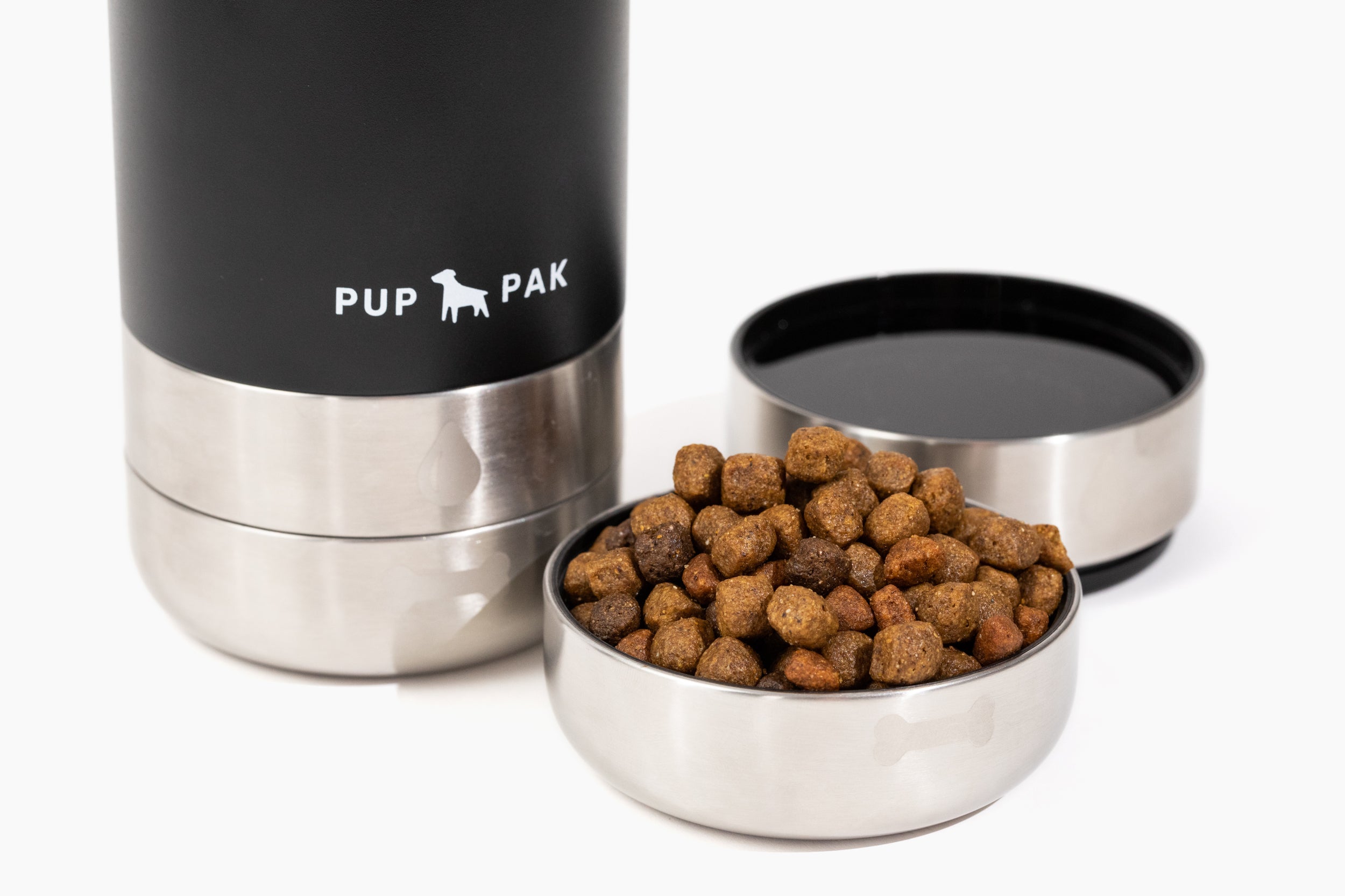 Close-up of the black Pup Pak dog water bottle with its detachable stainless steel bowls, one filled with water and the other with kibble. The bottle's design allows pet owners to easily provide food and hydration for their pets during travel and outdoor activities. The durable and portable Pup Pak ensures pets stay nourished and hydrated on the go, making it an essential accessory for active pet owners.