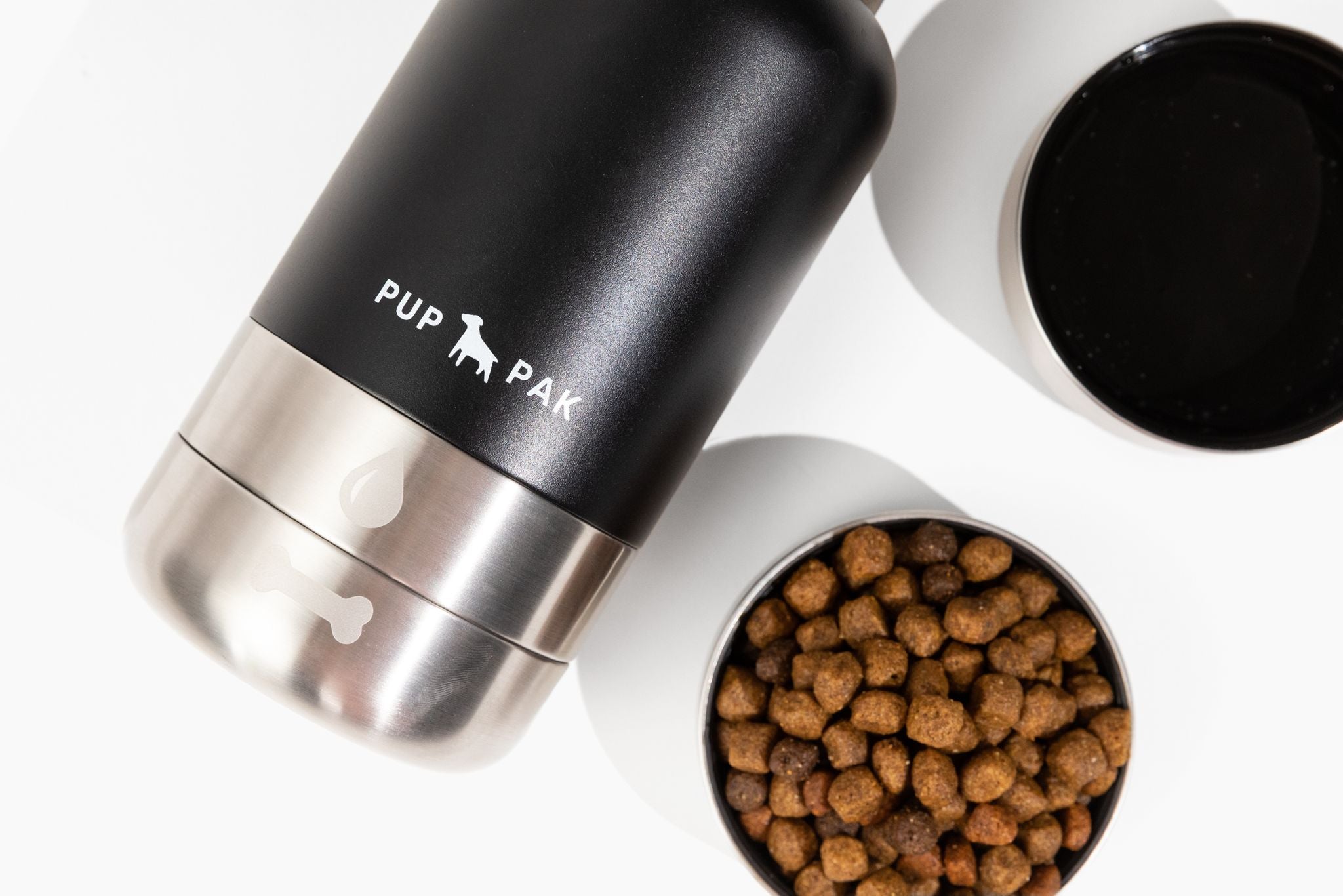 Close-up of the black Pup Pak dog water bottle with its detachable stainless steel bowls, one filled with water and the other with kibble. This innovative bottle design allows pet owners to easily provide food and hydration for their pets during travel and outdoor activities. The durable and portable Pup Pak ensures pets stay nourished and hydrated on the go, making it an essential accessory for active pet owners.